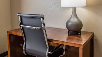 A hotel desk with a black leather chair and a modern table lamp.