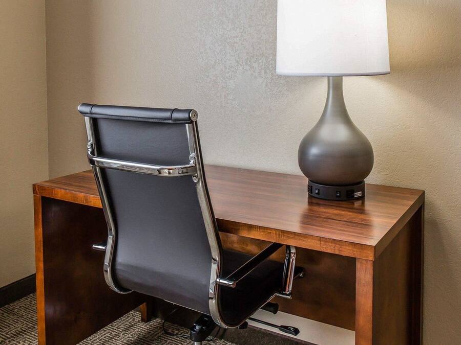 A hotel desk with a black leather chair and a modern table lamp.