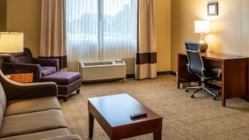 A hotel room with a sofa, armchair, desk, and lamp.