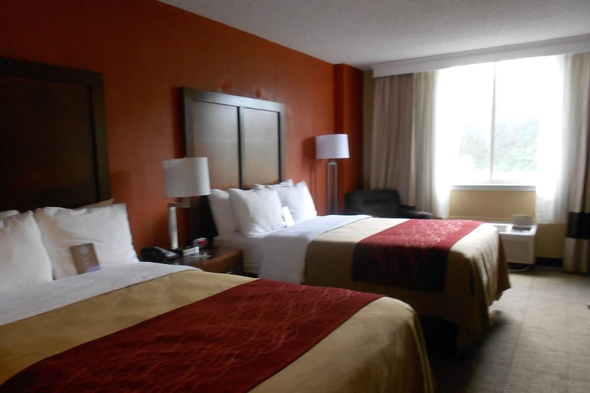 Een hotelkamer met twee bedden, een bureau, een stoel, een lamp en een raam met gordijnen.