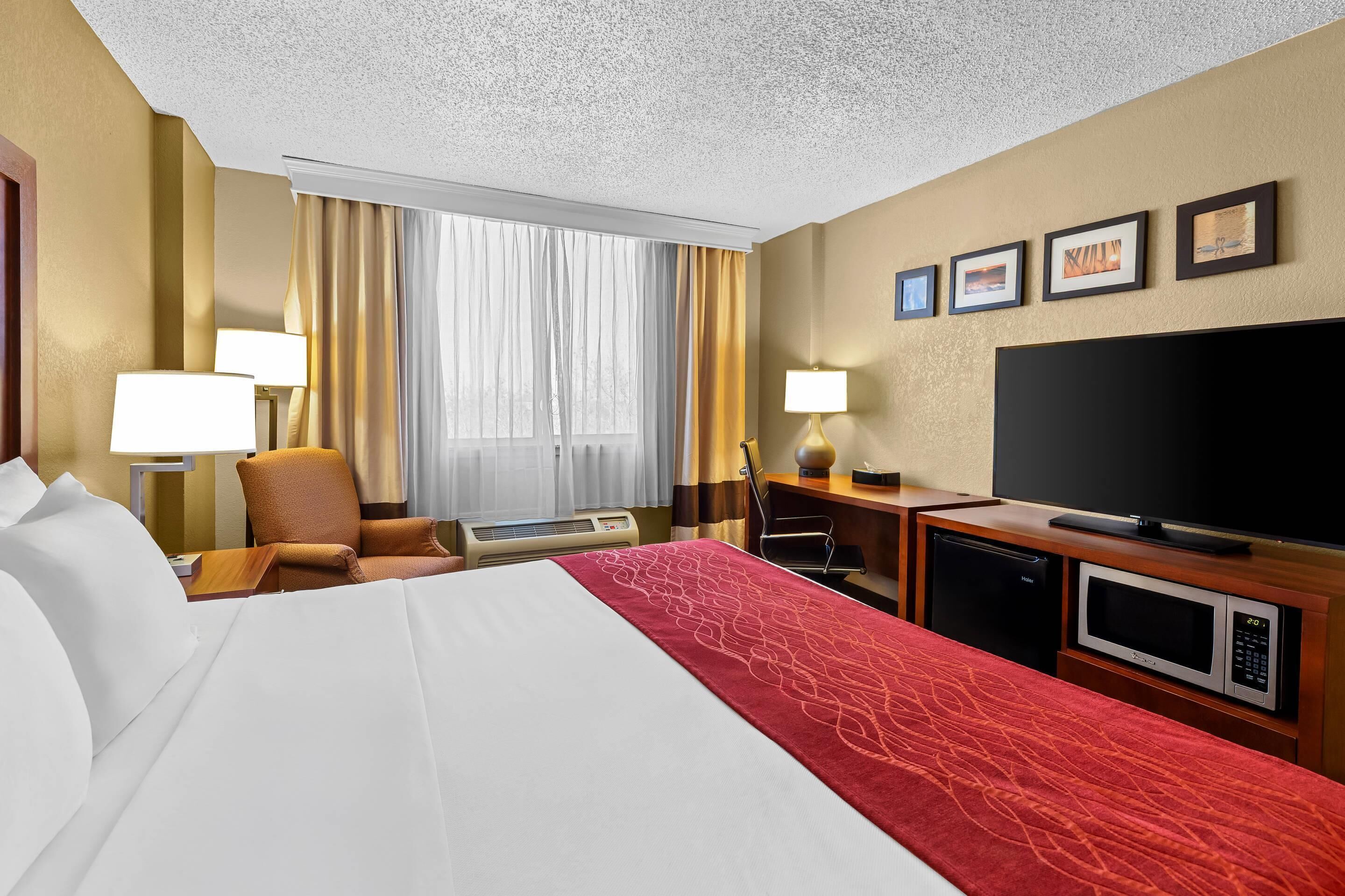 A hotel room with a bed, a desk, a television, a microwave, and a window with curtains.