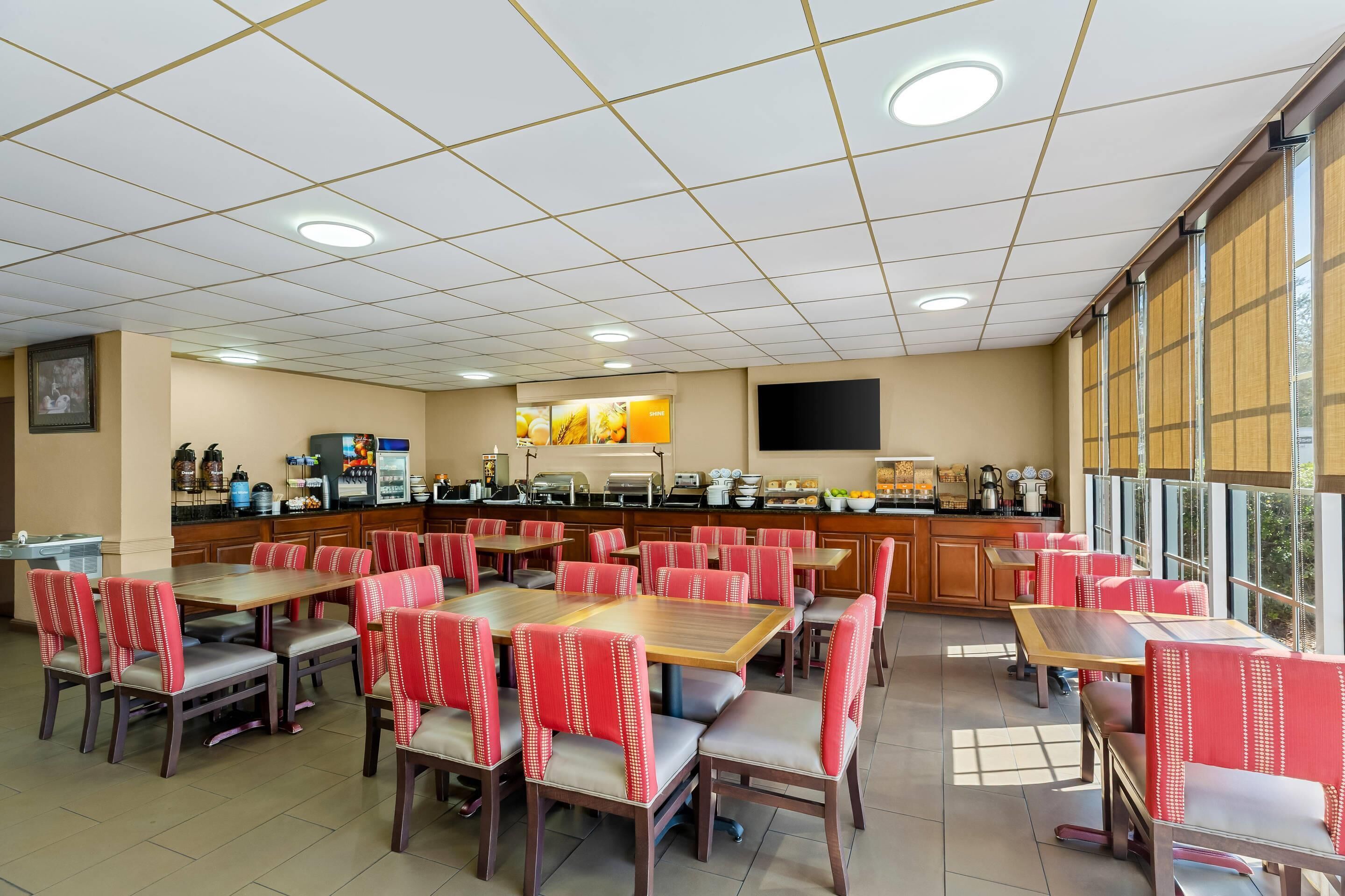 A restaurant with multiple tables and chairs, a kitchen area, and large windows.