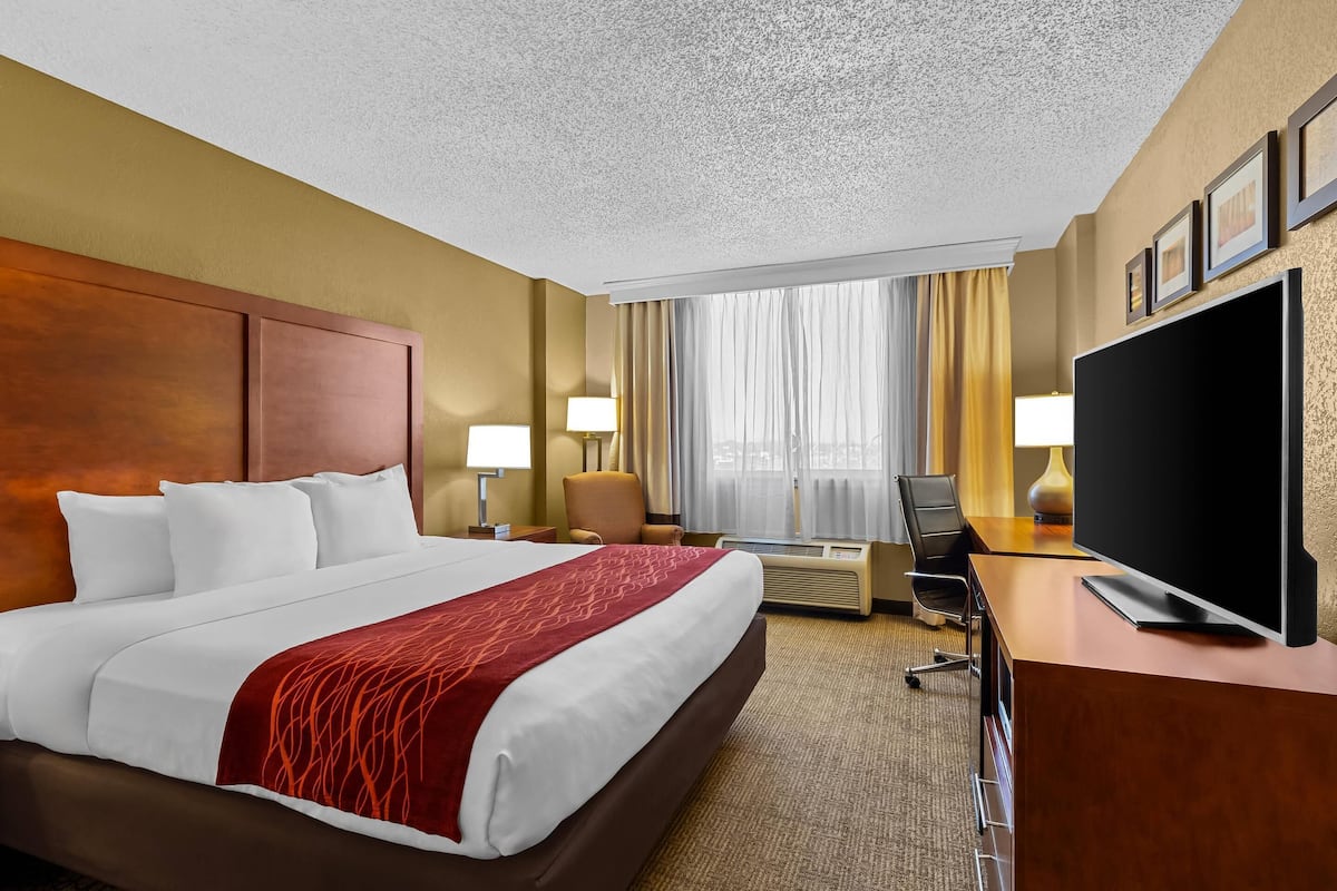 Een hotelkamer met een groot bed, een bureau met een flatscreen televisie, een stoel, een bureaulamp en een raam met gordijnen.
