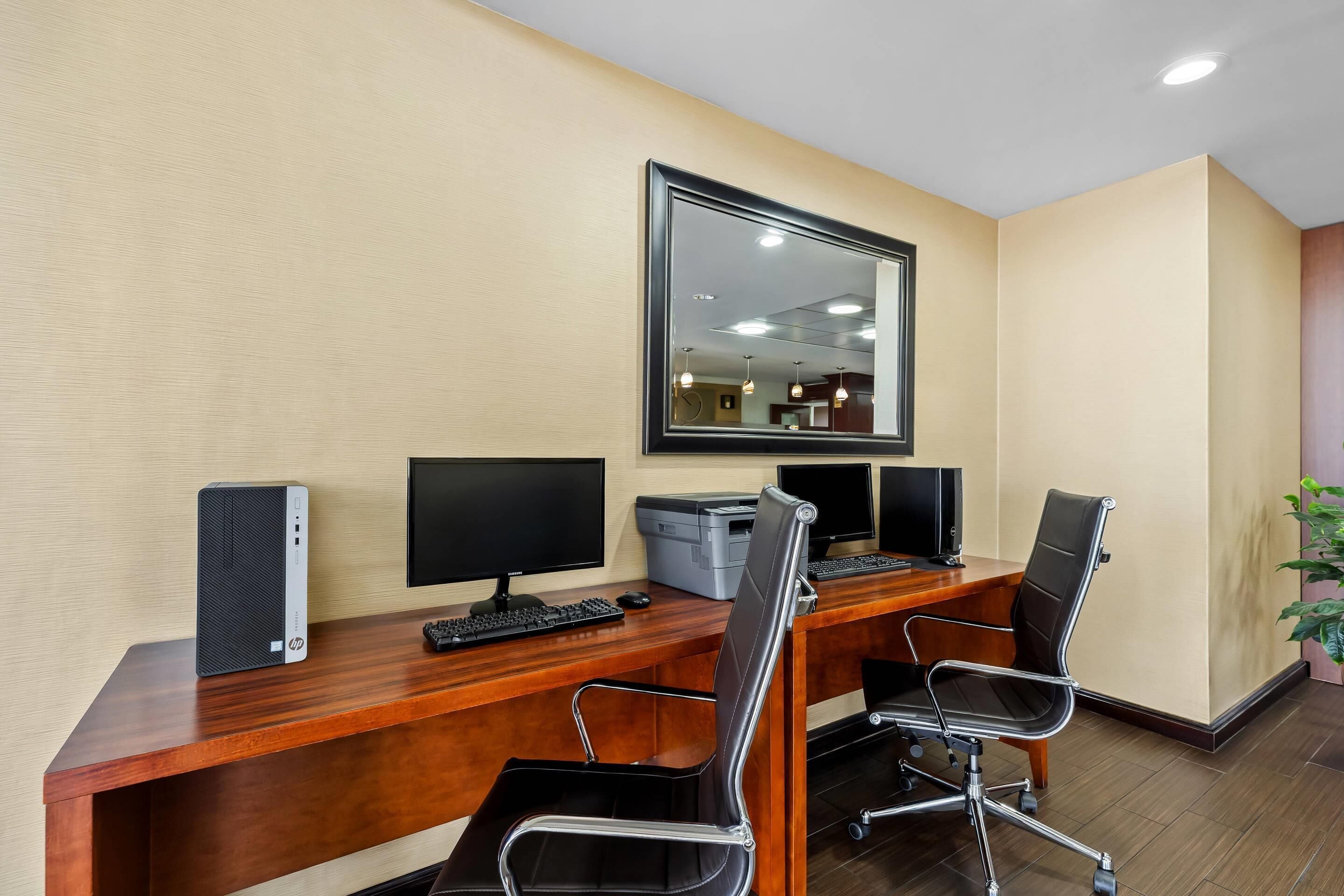 A conference room with a wooden desk, two black office chairs, a desktop computer, a monitor, a keyboard, and a printer.