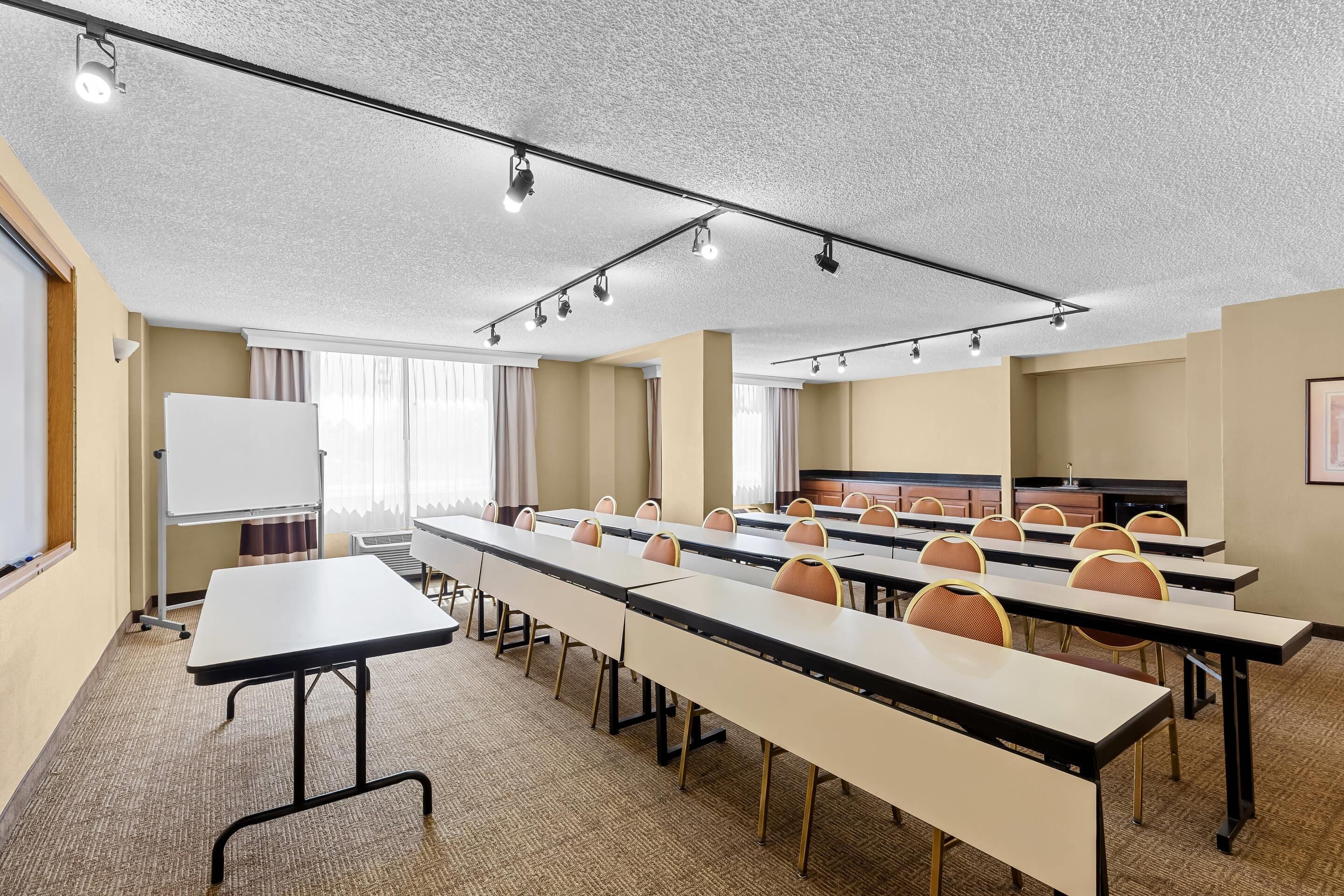 Une salle de conférence équipée de longues tables, de chaises, d’un tableau blanc et d’un téléviseur.