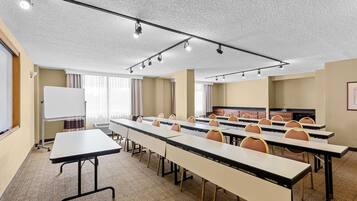 Une salle de conférence équipée de longues tables, de chaises, d’un tableau blanc et d’un téléviseur.