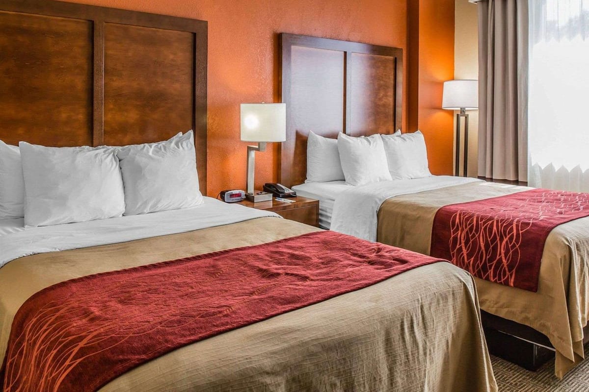 Een hotelkamer met twee bedden, een nachtkastje met lamp en een raam met gordijnen.