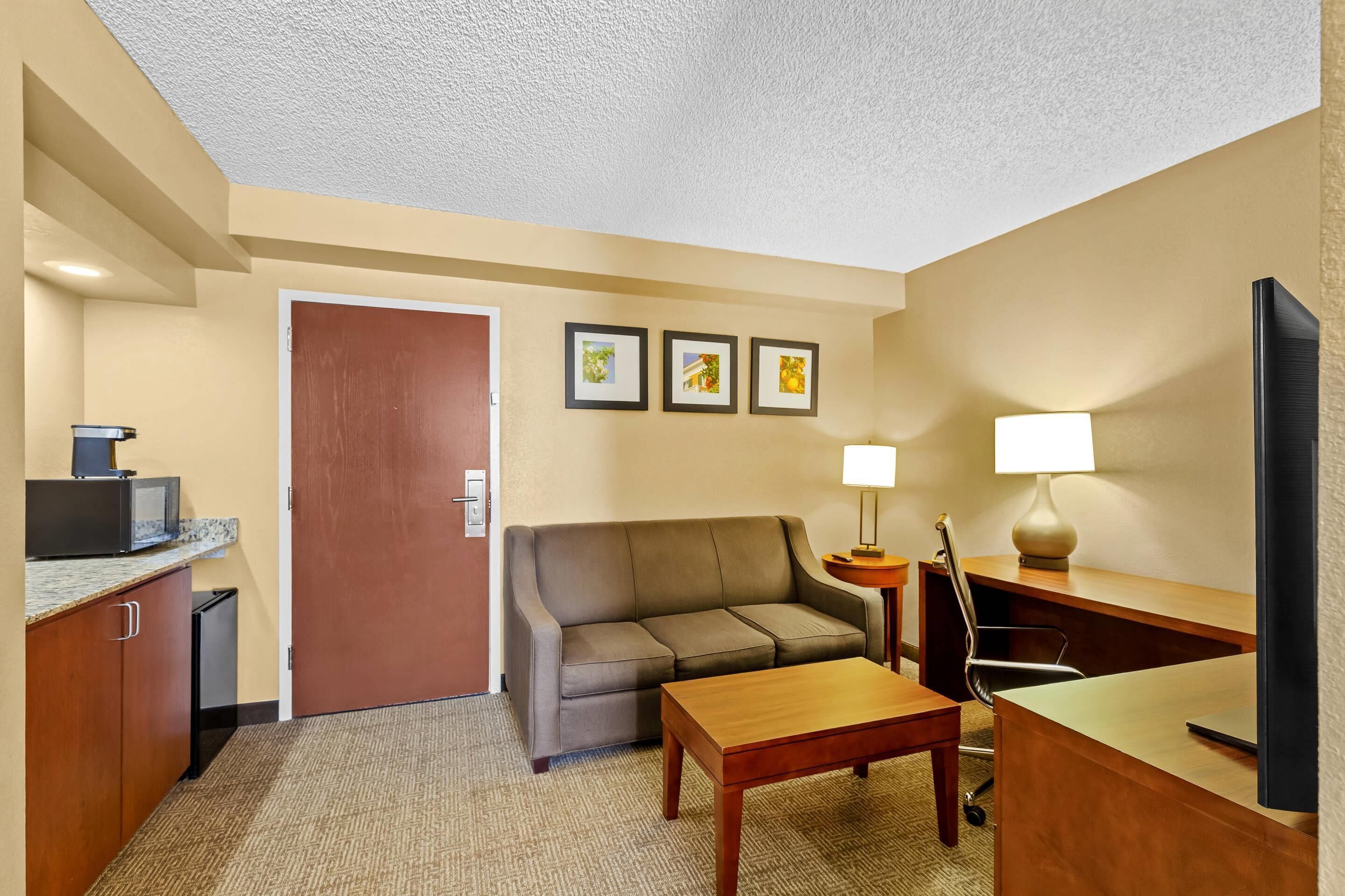 A hotel room with a sofa, a small table, a TV, a desk, a lamp, and a microwave.