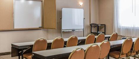 Een vergaderruimte met een lange tafel, meerdere stoelen, een whiteboard en een beamerstandaard.