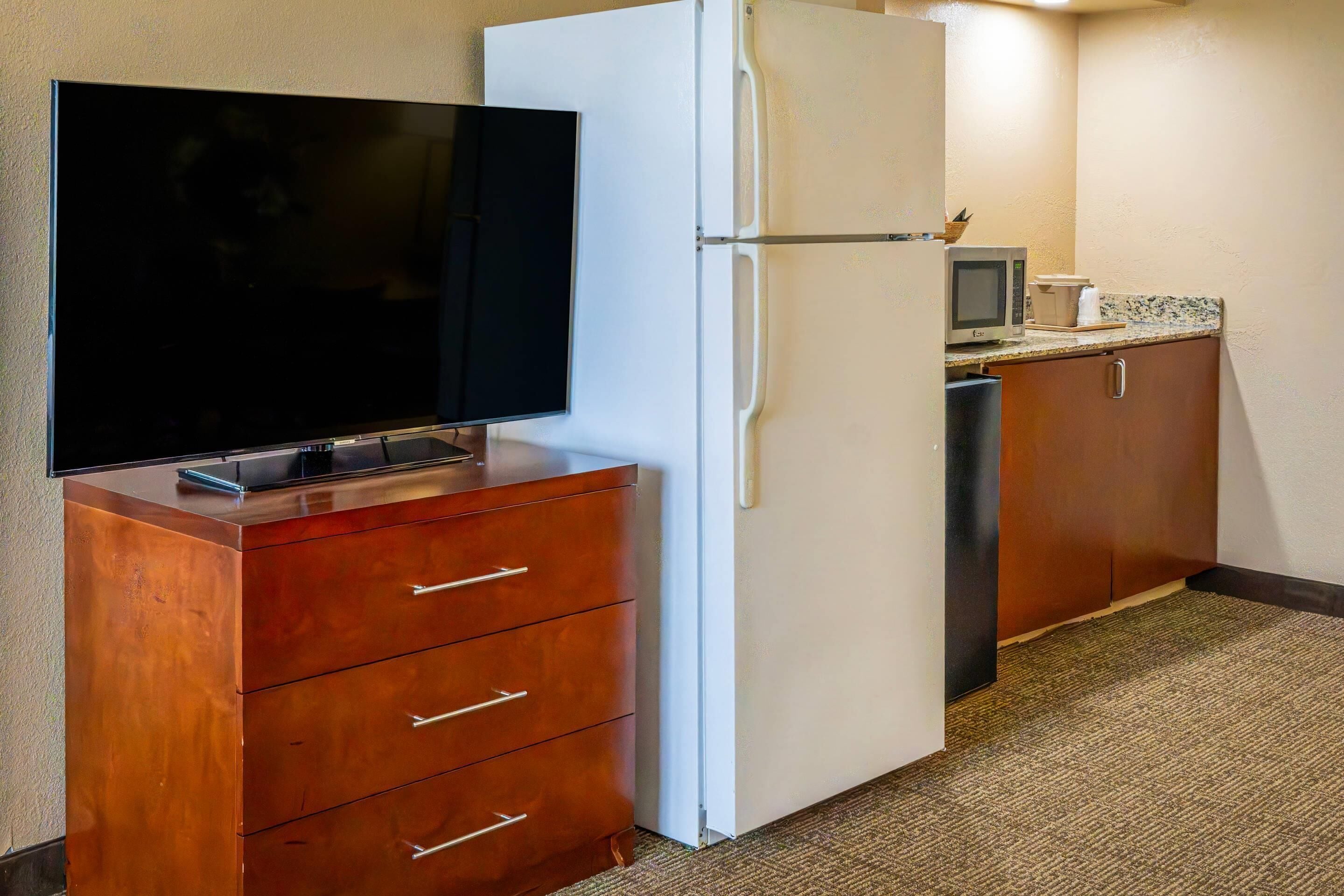 Een compacte kitchenette met een flatscreen televisie, een witte koelkast, een magnetron en een klein aanrecht.