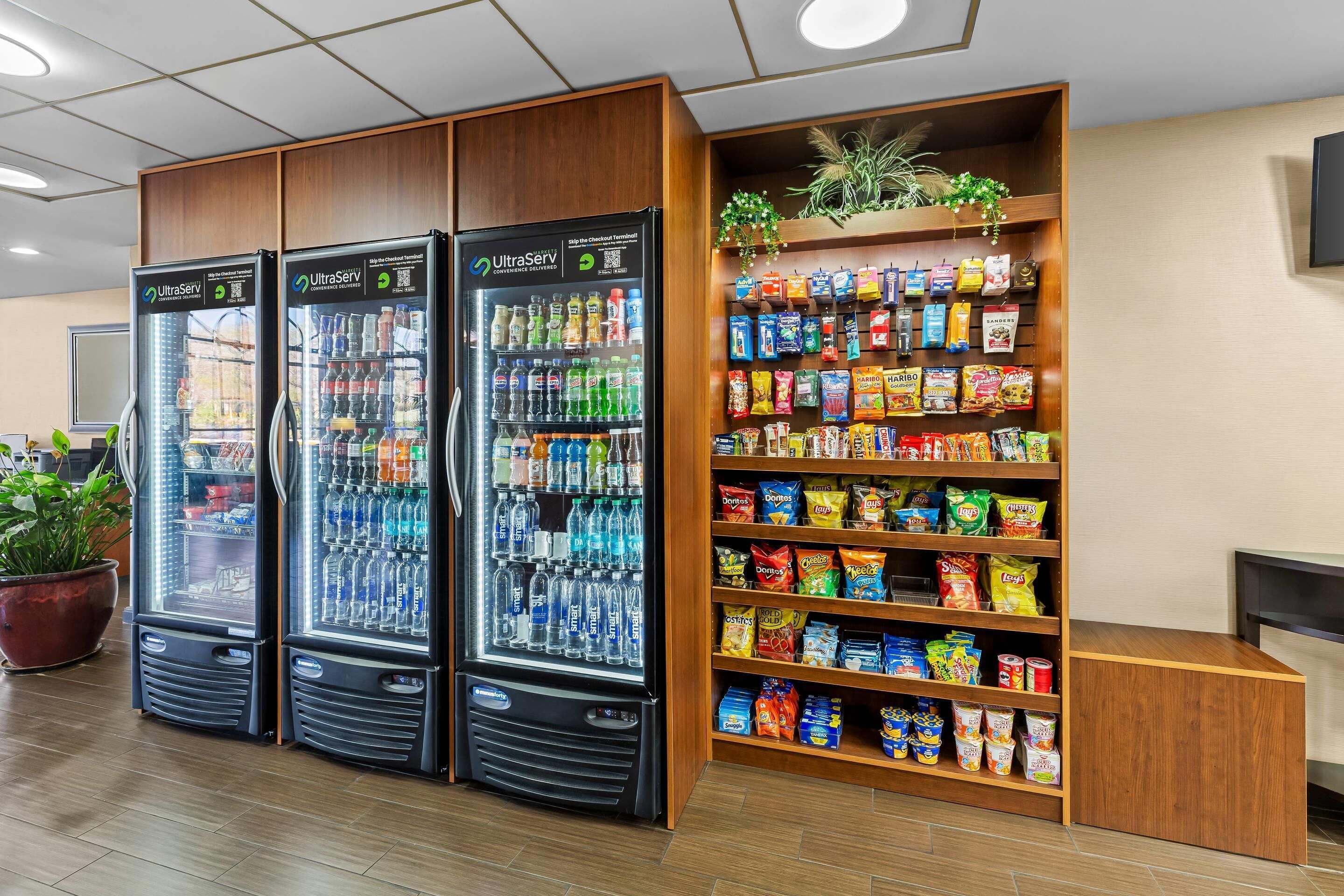 A vending area with three refrigerated beverage dispensers and a shelf stocked with snacks and drinks.