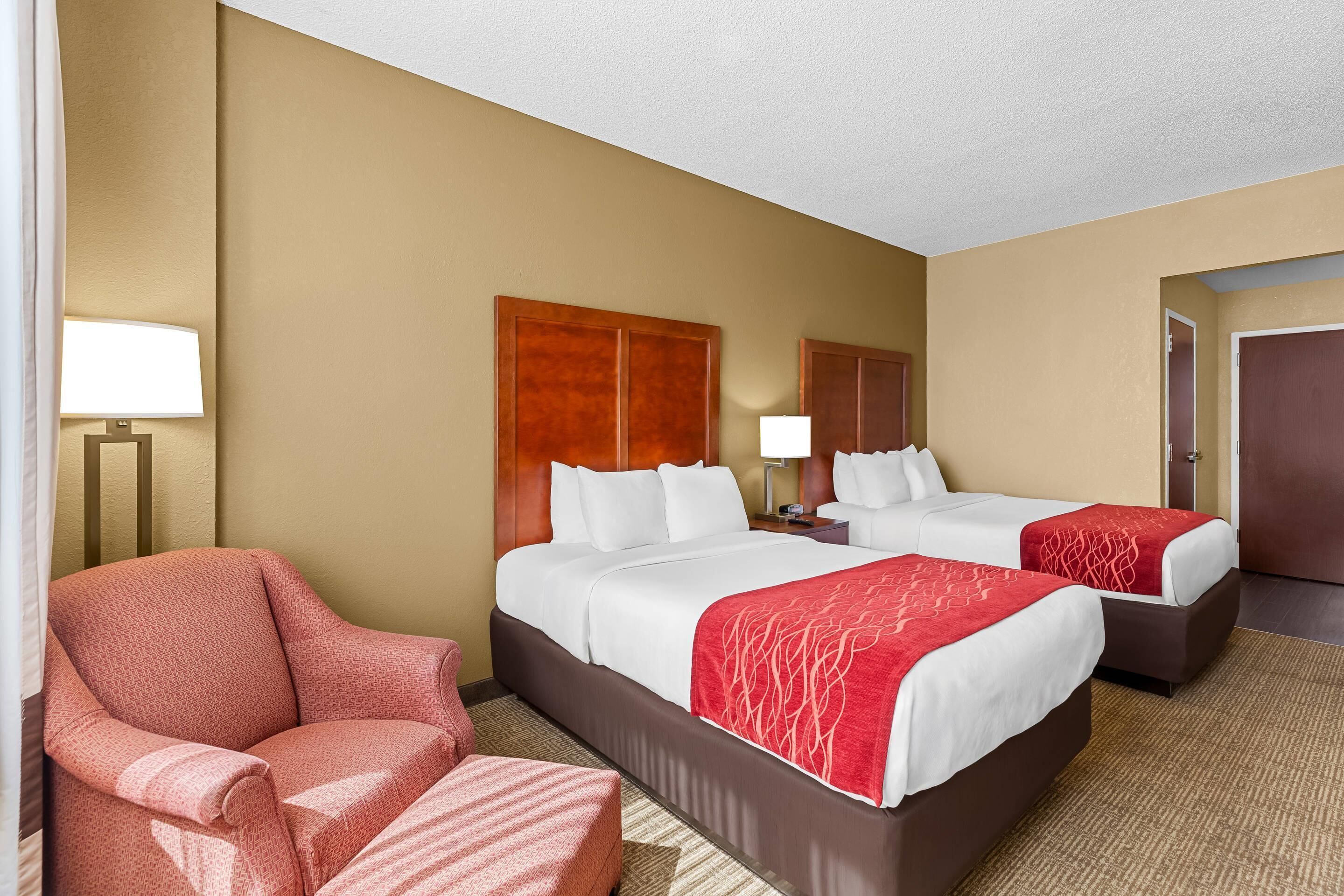 A hotel room with two beds, a chair, a nightstand, and a lamp.