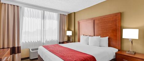 Habitación de hotel con una cama grande, dos mesitas de noche con lámparas, cabecero de madera, ventana con cortinas y suelo alfombrado.