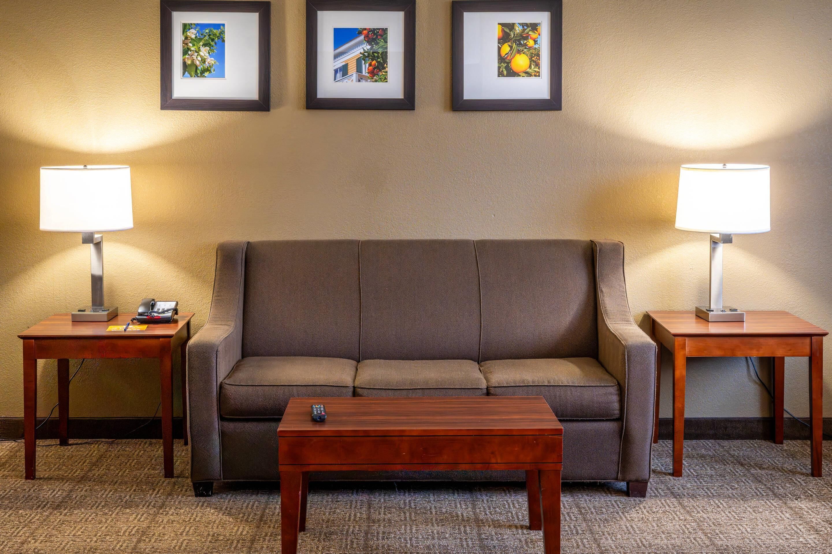 Habitación de hotel con sofá marrón, dos mesitas de noche con lámparas, una mesa de centro de madera y tres cuadros enmarcados en la pared.