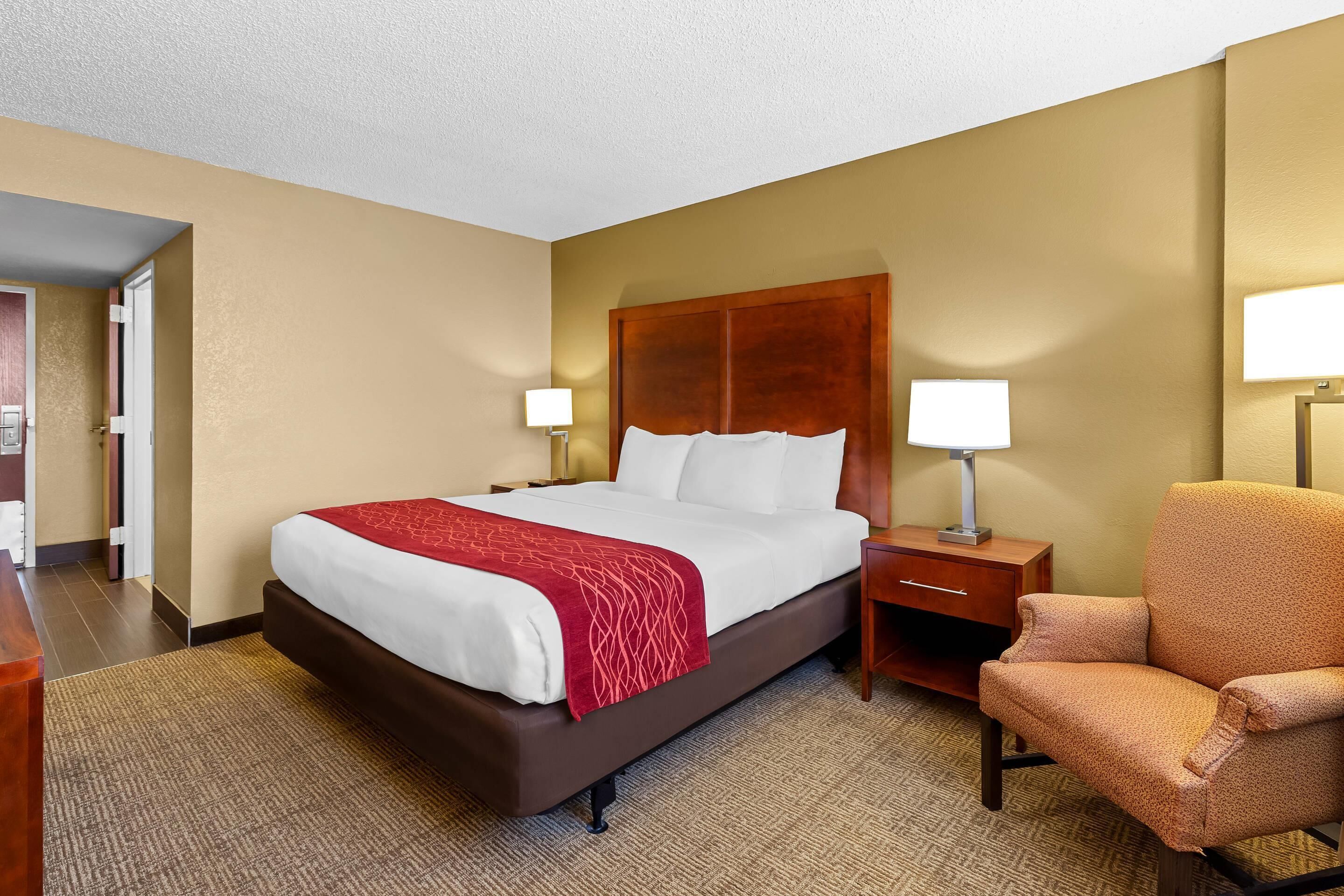 A hotel room with a bed, nightstand, chair, and a lamp.
