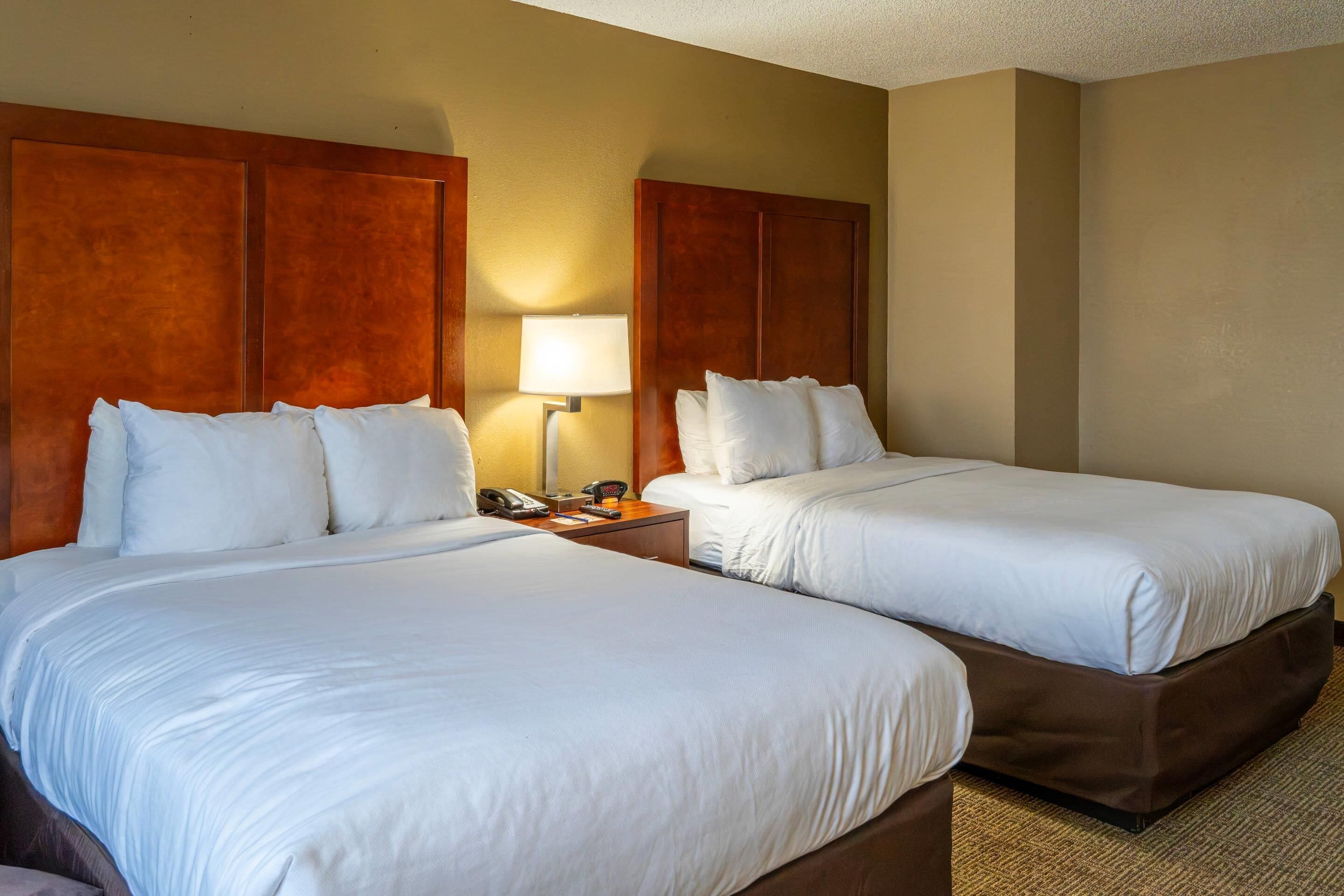 A hotel room with two beds, a nightstand with a lamp, and a telephone.