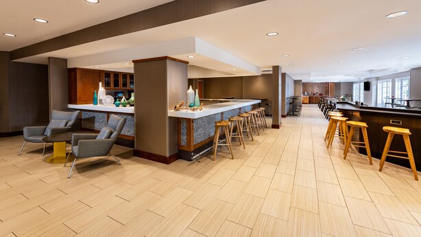 A modern kitchen with a bar area, wooden stools, and a seating area with chairs.
