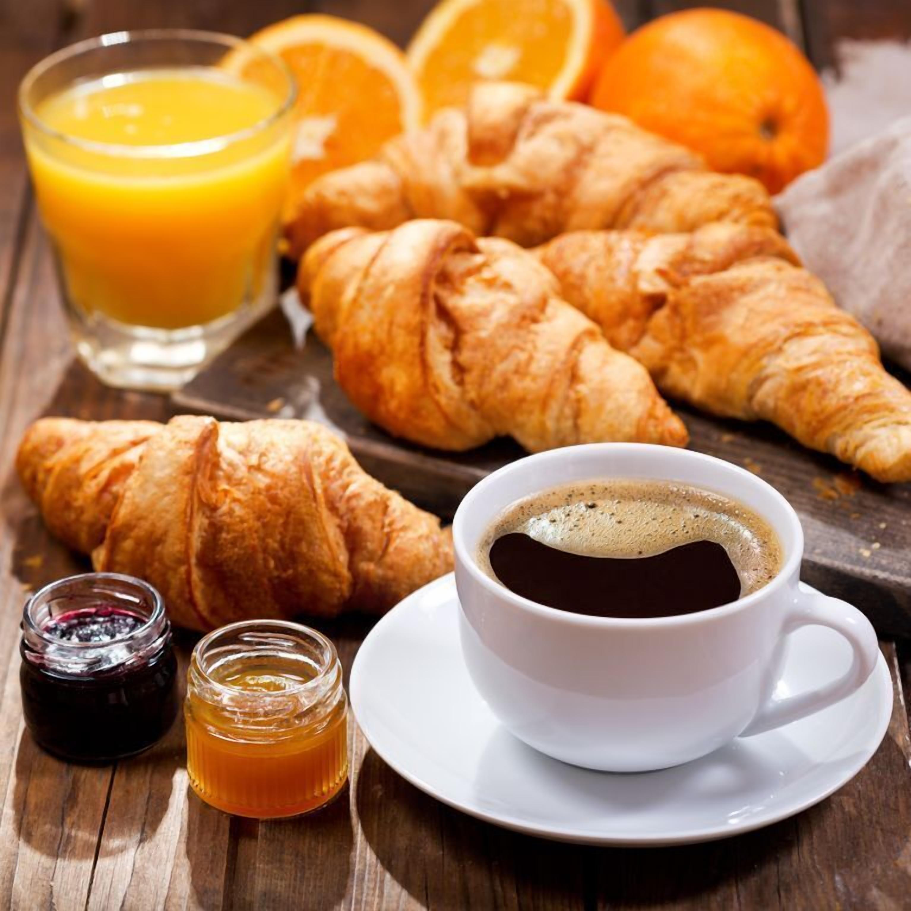 Desayuno con cruasanes, zumo de naranja, café y miel sobre una mesa de madera.