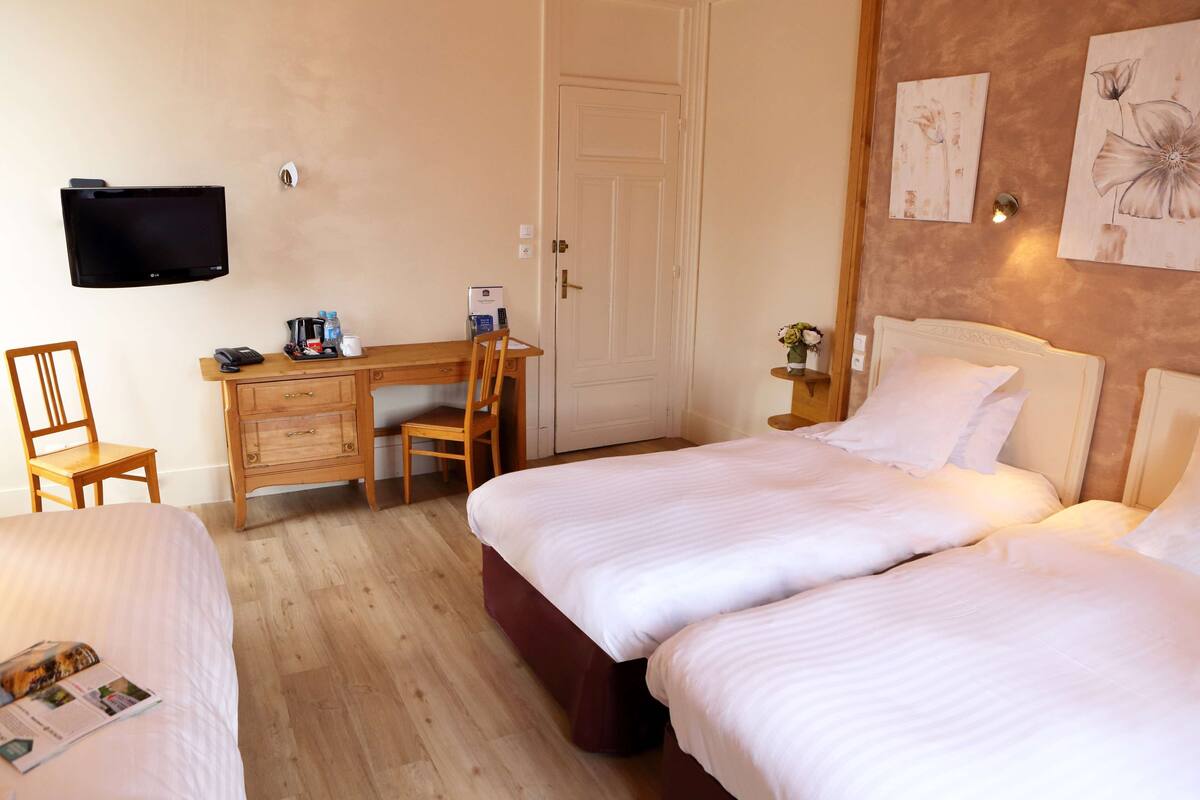 A hotel room with two beds, a desk with a chair, a TV mounted on the wall, and artwork on the wall.