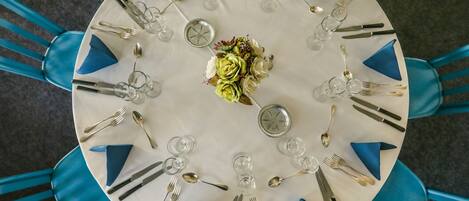 A round table set for a meal with blue napkins, silverware, and a floral centerpiece.