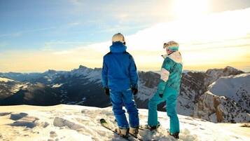 Two people standing on a snowy mountain peak with a view of distant mountains and a clear sky.