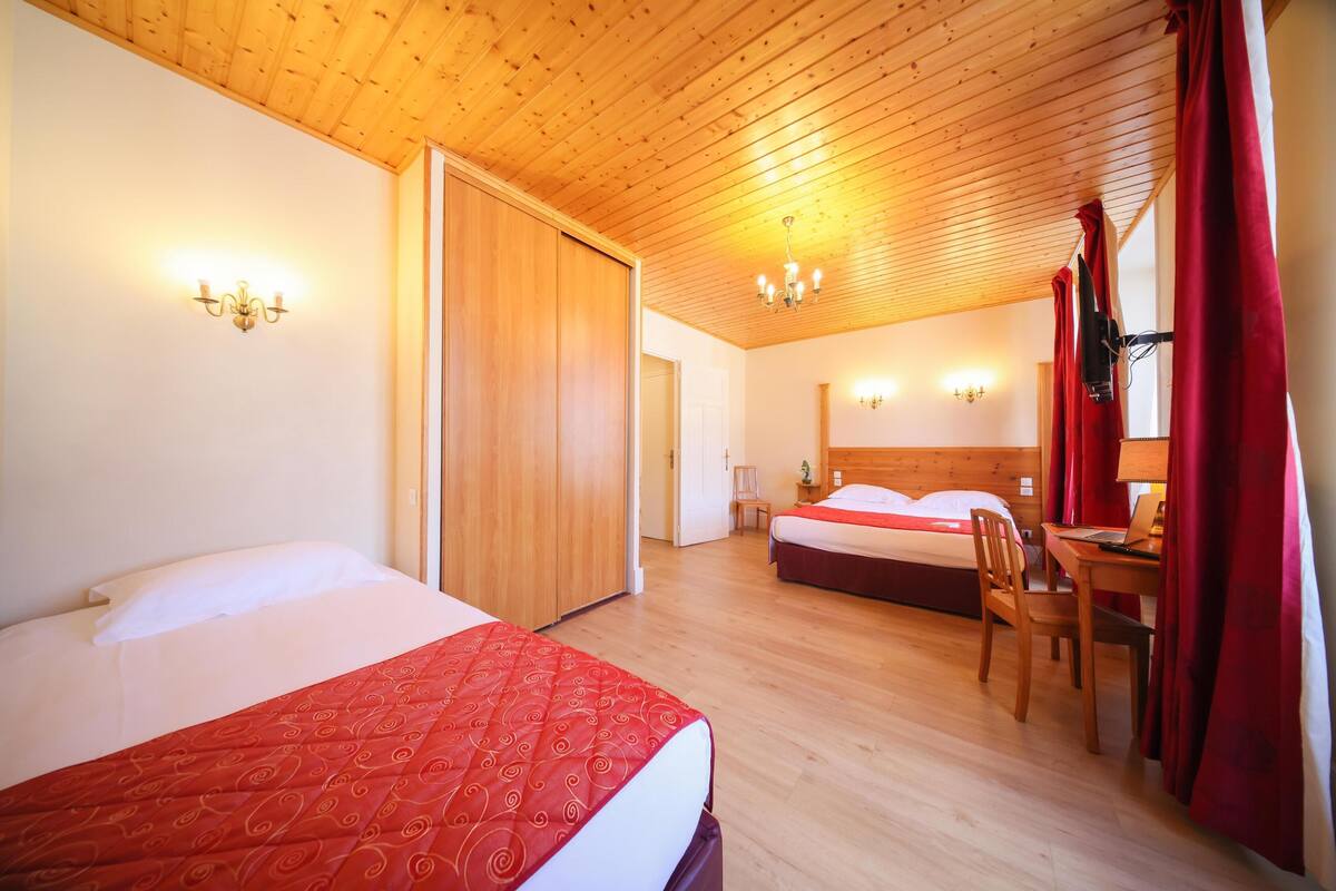 A hotel room with two beds, wooden ceiling, and a desk with a chair.