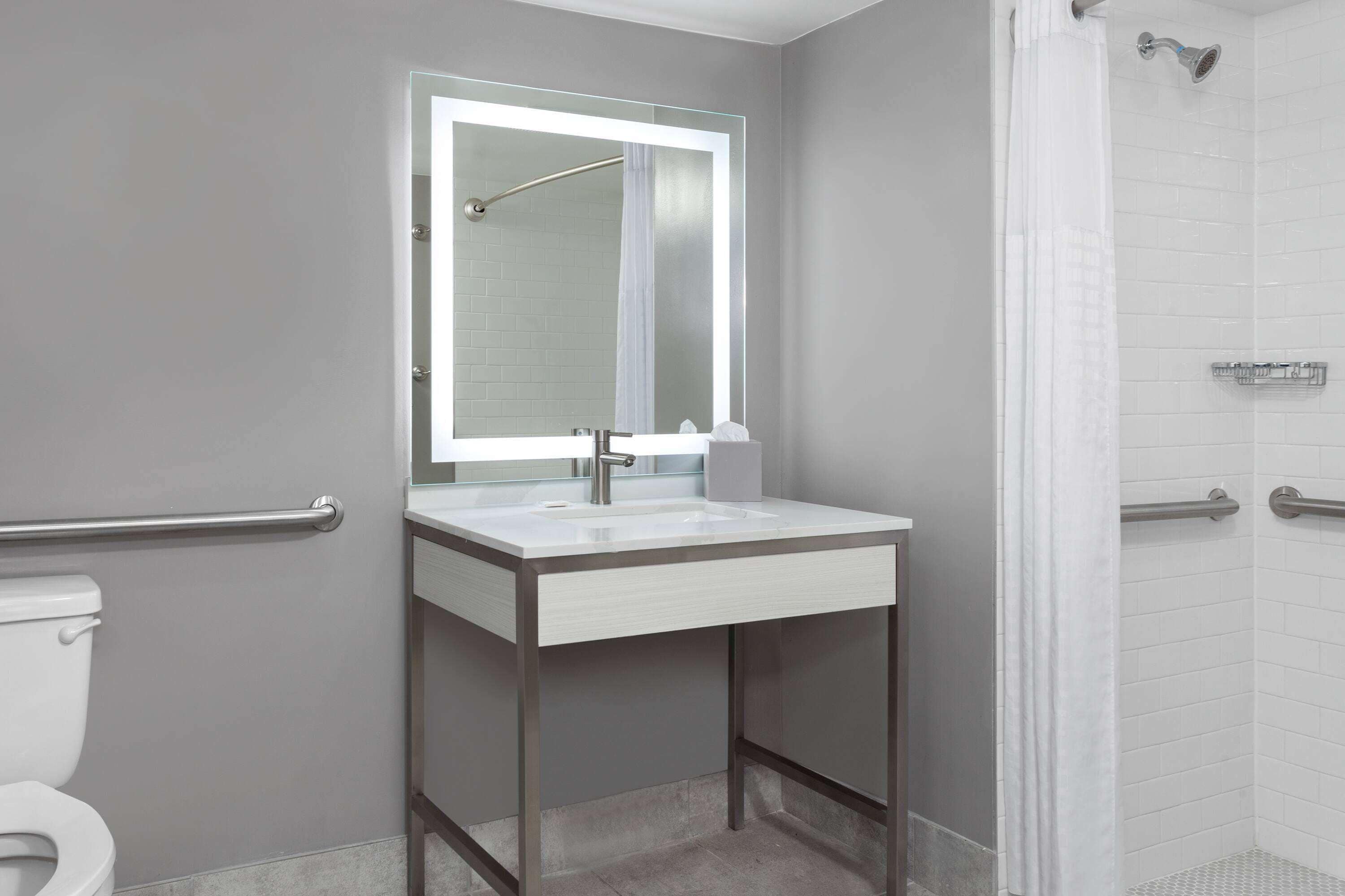 Un baño moderno con lavamanos, espejo y ducha blancos.
