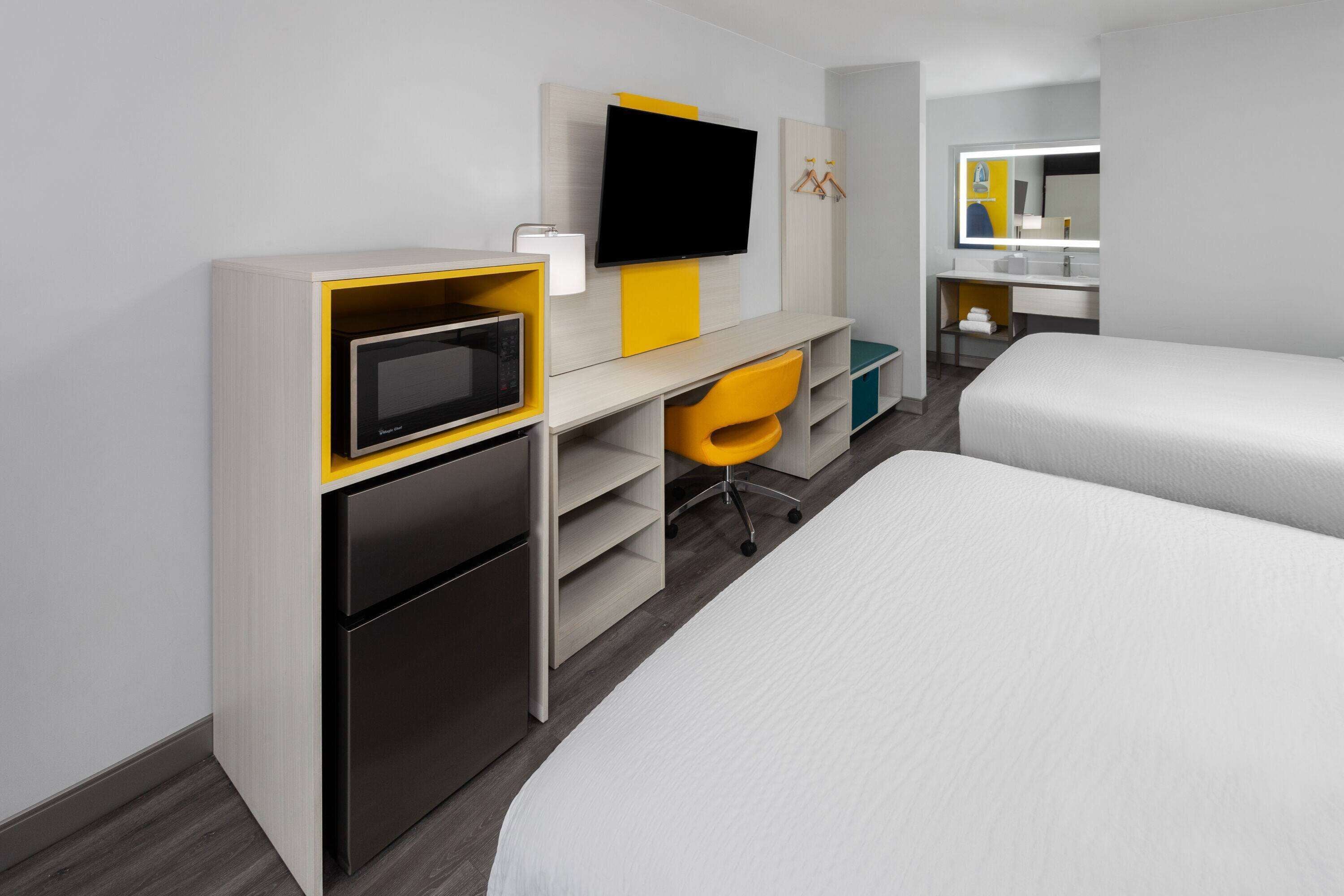 A hotel room with a bed, a desk with a TV, a mini-fridge, and a chair.
