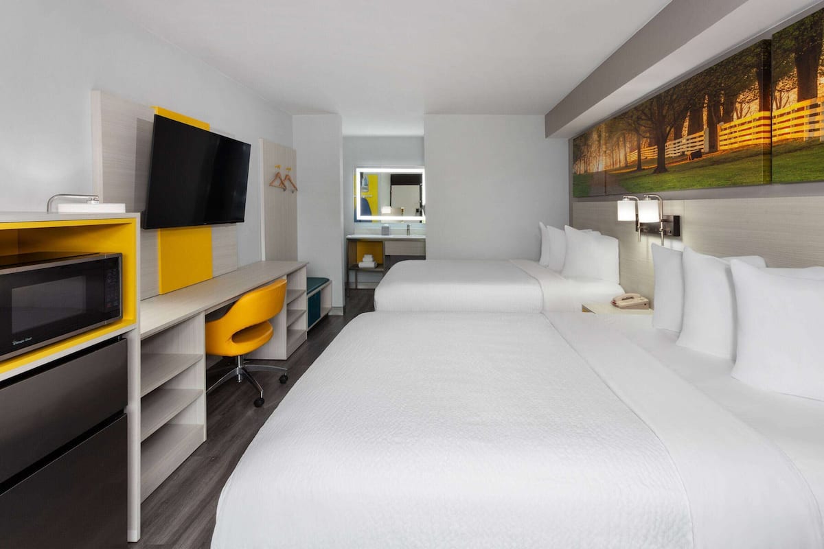 A hotel room with a large bed, a TV, a desk, and a bathroom visible through an open door.
