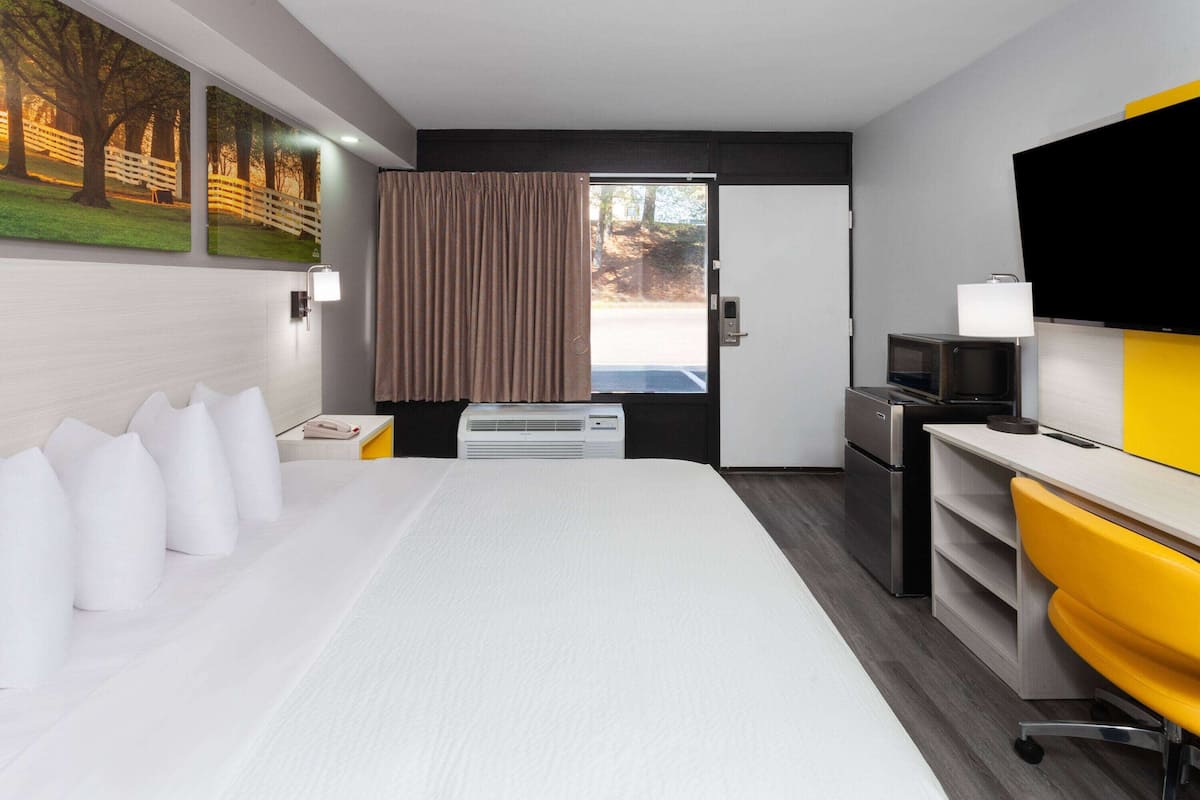 A hotel room with a bed, a desk with a TV, a microwave, and a window with curtains.