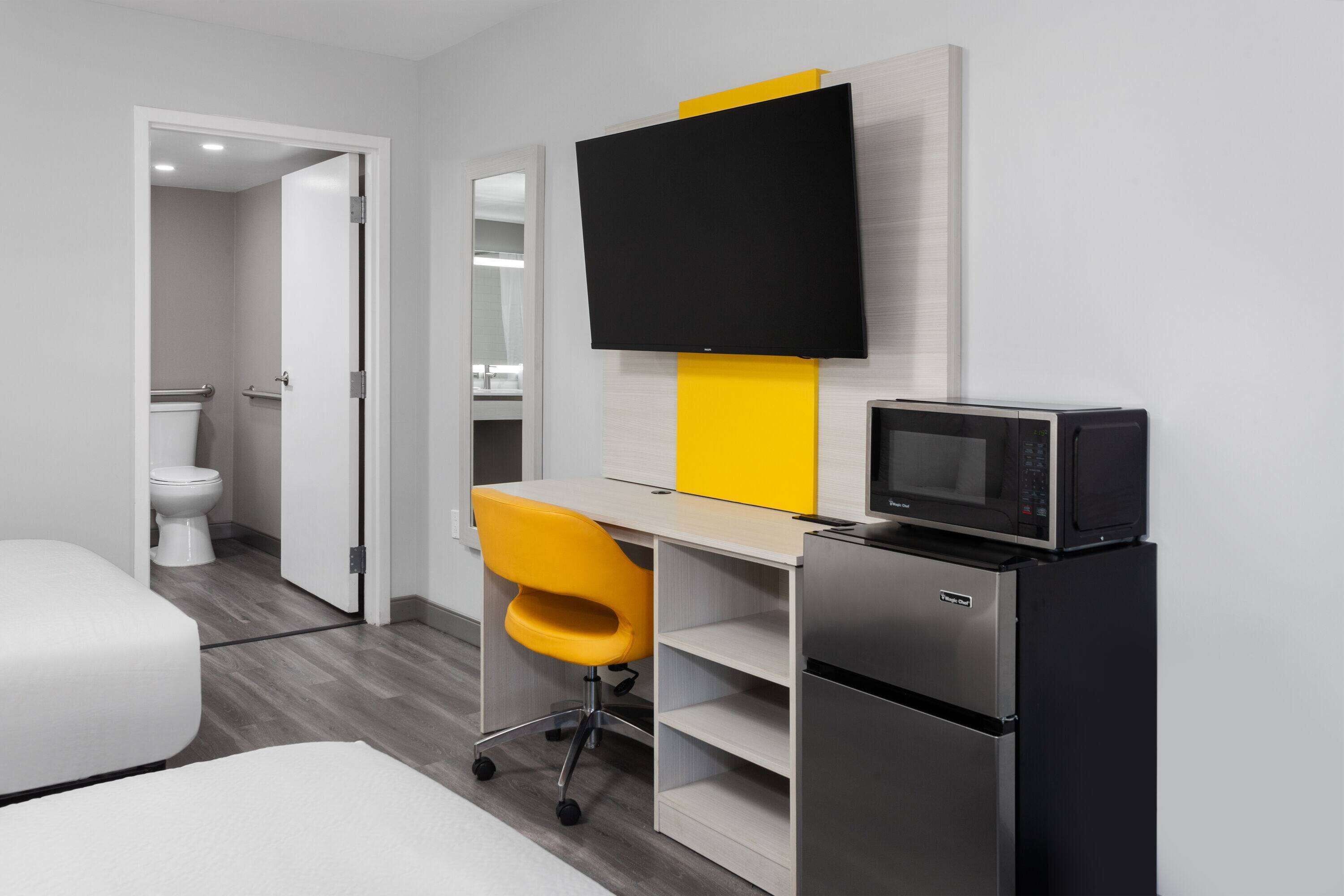 A modern hotel room with a bed, a desk with a chair, a flat-screen TV, a microwave, and a refrigerator.