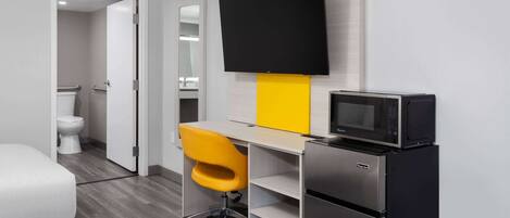 A modern hotel room with a bed, a desk with a chair, a flat-screen TV, a microwave, and a refrigerator.
