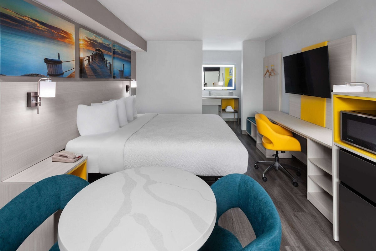 A modern hotel room with a large bed, a desk with a chair, a TV, and a dining table.