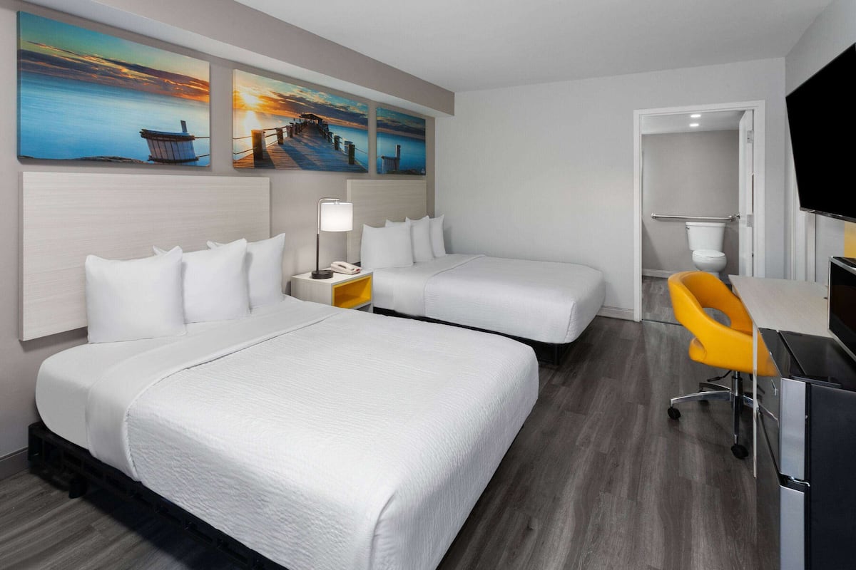 A hotel room with two beds, a desk, a chair, and artwork on the wall.