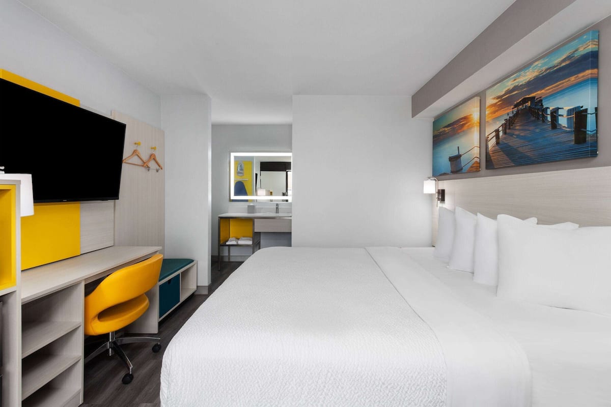 A modern hotel room with a large bed, a desk with a chair, a flat-screen TV, and artwork on the walls.