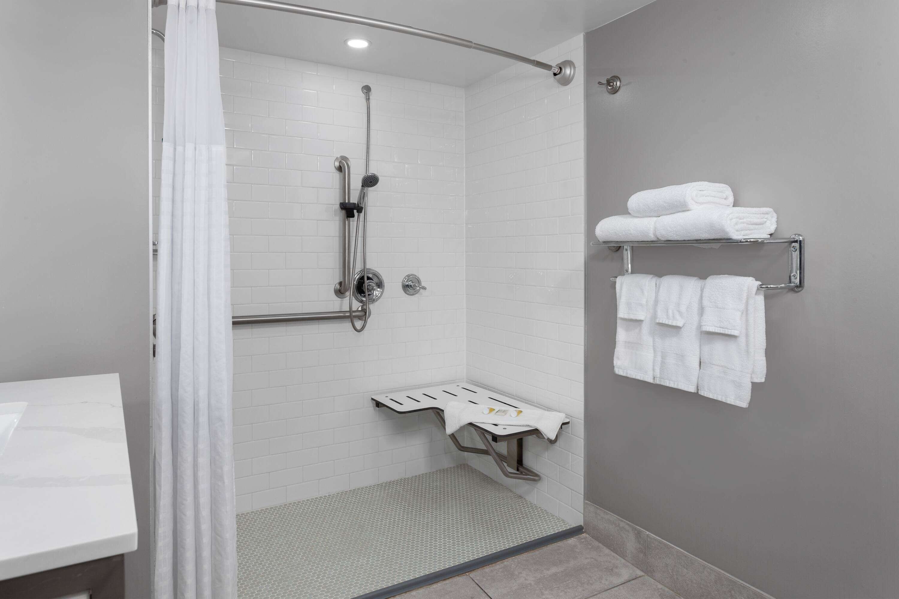 Une salle de bain moderne dotée d’une douche à l’italienne, d’une barre d’appui et d’un porte-serviettes où sont rangées des serviettes pliées avec soin.