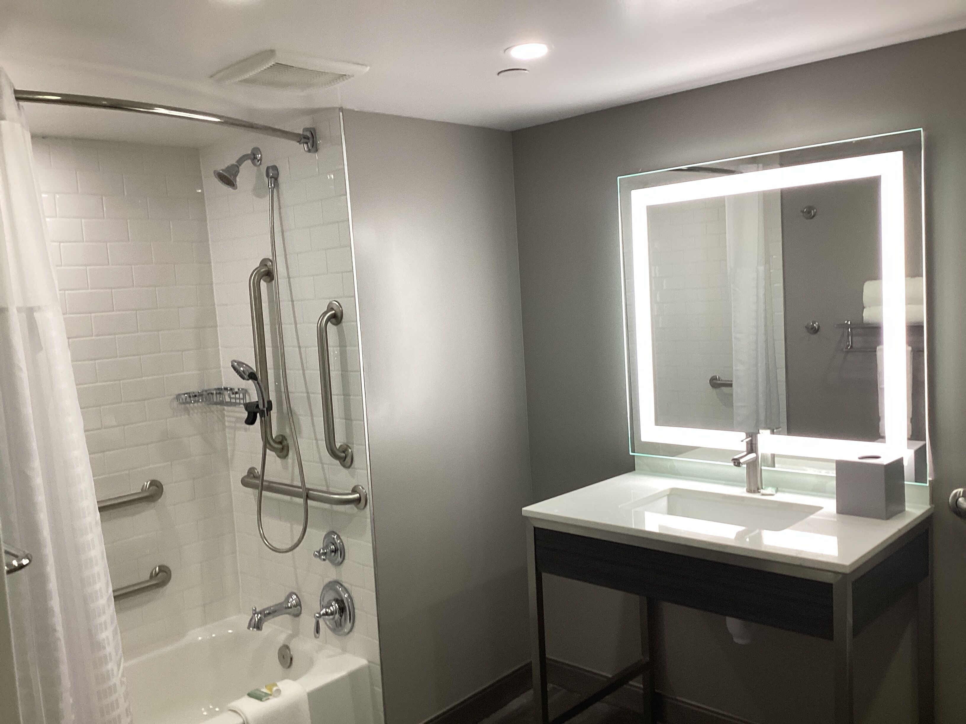 A modern bathroom with a glass-enclosed shower, a vanity with a large mirror, and a bathtub.