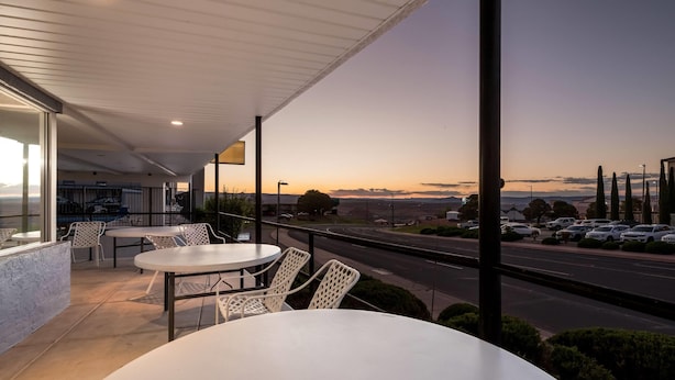 A balcony with white tables and chairs, overlooking a parking lot and a road with a sunset view. - Travelodge by Wyndham Page, View of Lake Powell (Page)