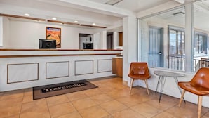 A reception area with a white reception desk, a monitor, a poster, and a view of the outside through large windows. - Travelodge by Wyndham Page, View of Lake Powell (Page)