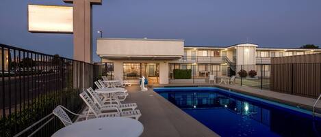 A Travelodge by Wyndham with a swimming pool, outdoor seating, and a well-lit entrance.