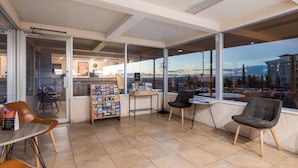 A modern indoor space with a glass wall, a small seating area with chairs, a table, and a magazine rack. - Travelodge by Wyndham Page, View of Lake Powell (Page)