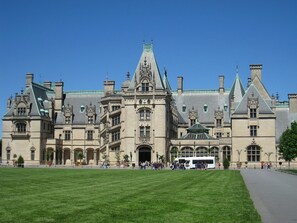 Ein großes, historisches Gebäude mit einem zentralen Eingang, mehreren Flügeln und einem gepflegten Rasen davor.