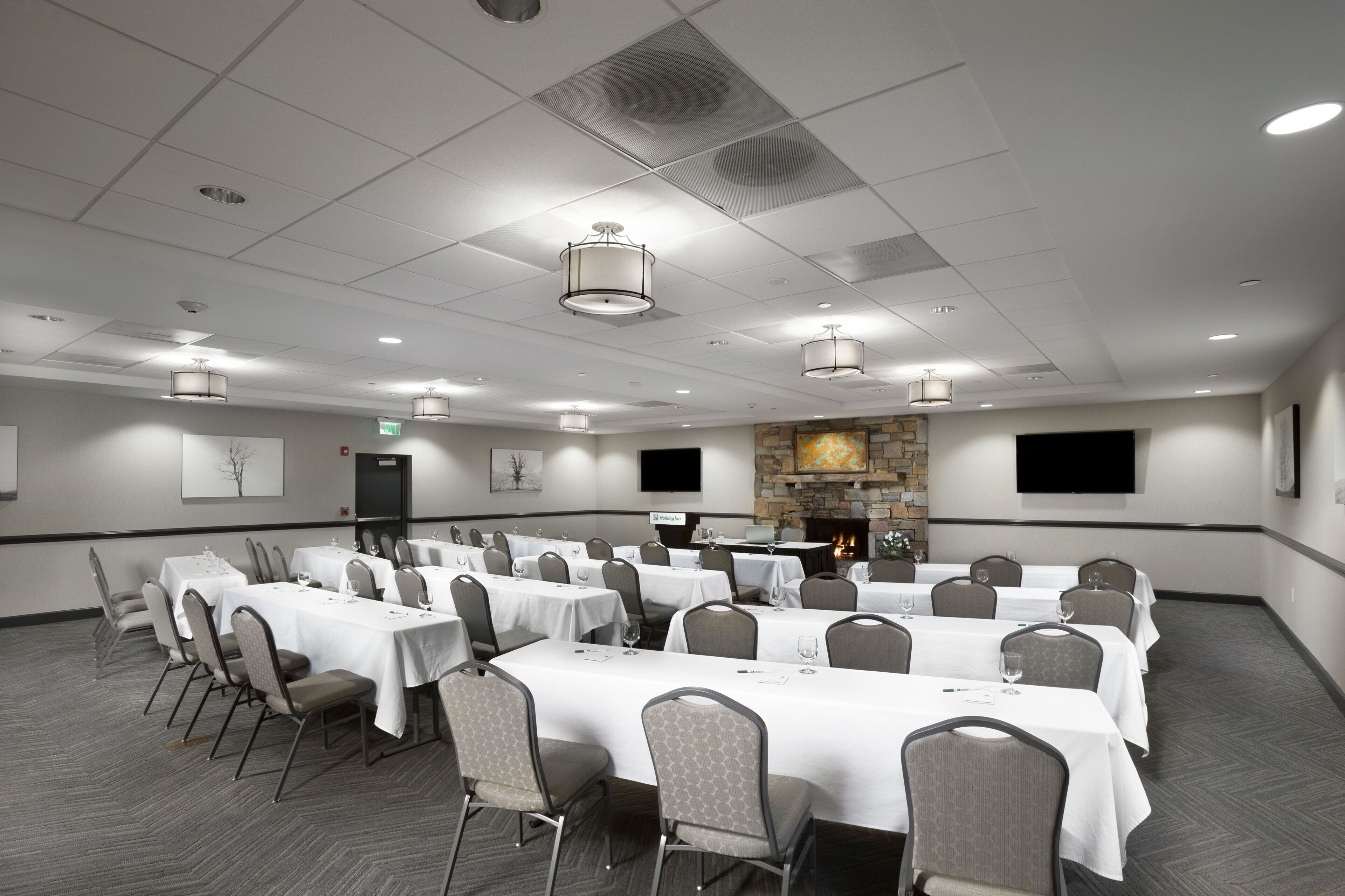 A conference room with multiple tables and chairs, a fireplace, and a flat-screen TV on the wall.