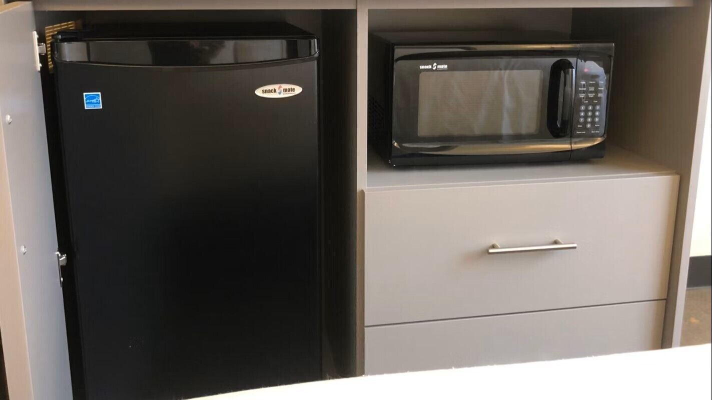A black refrigerator and a microwave on a cabinet shelf.