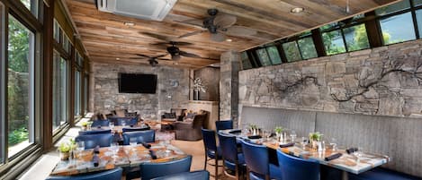 Un restaurante con pared de piedra, techo de madera y ventanas amplias.