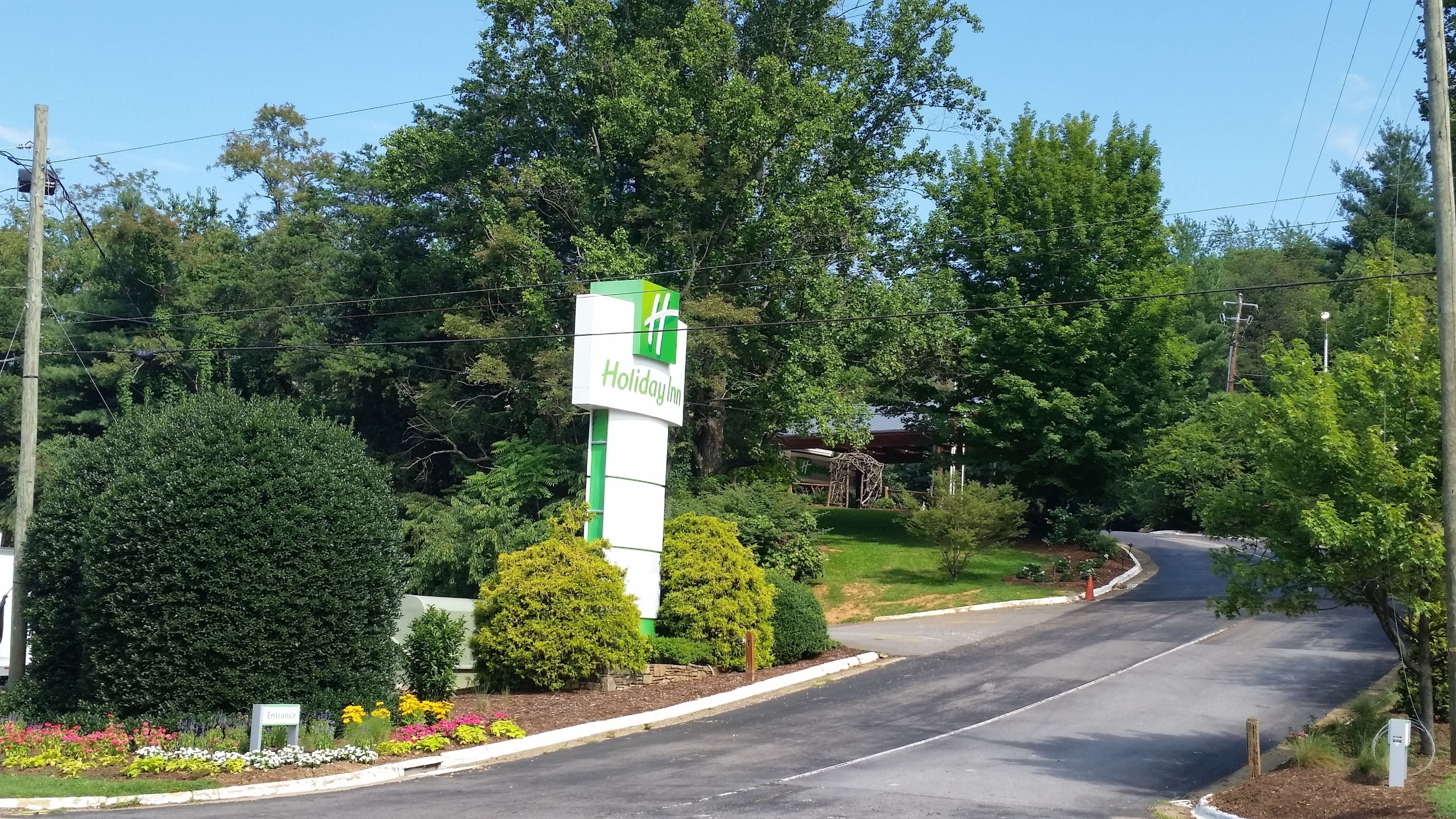 Señal de Holiday Inn con un esquema de color verde y blanco, rodeada de exuberante follaje y un césped cuidado.