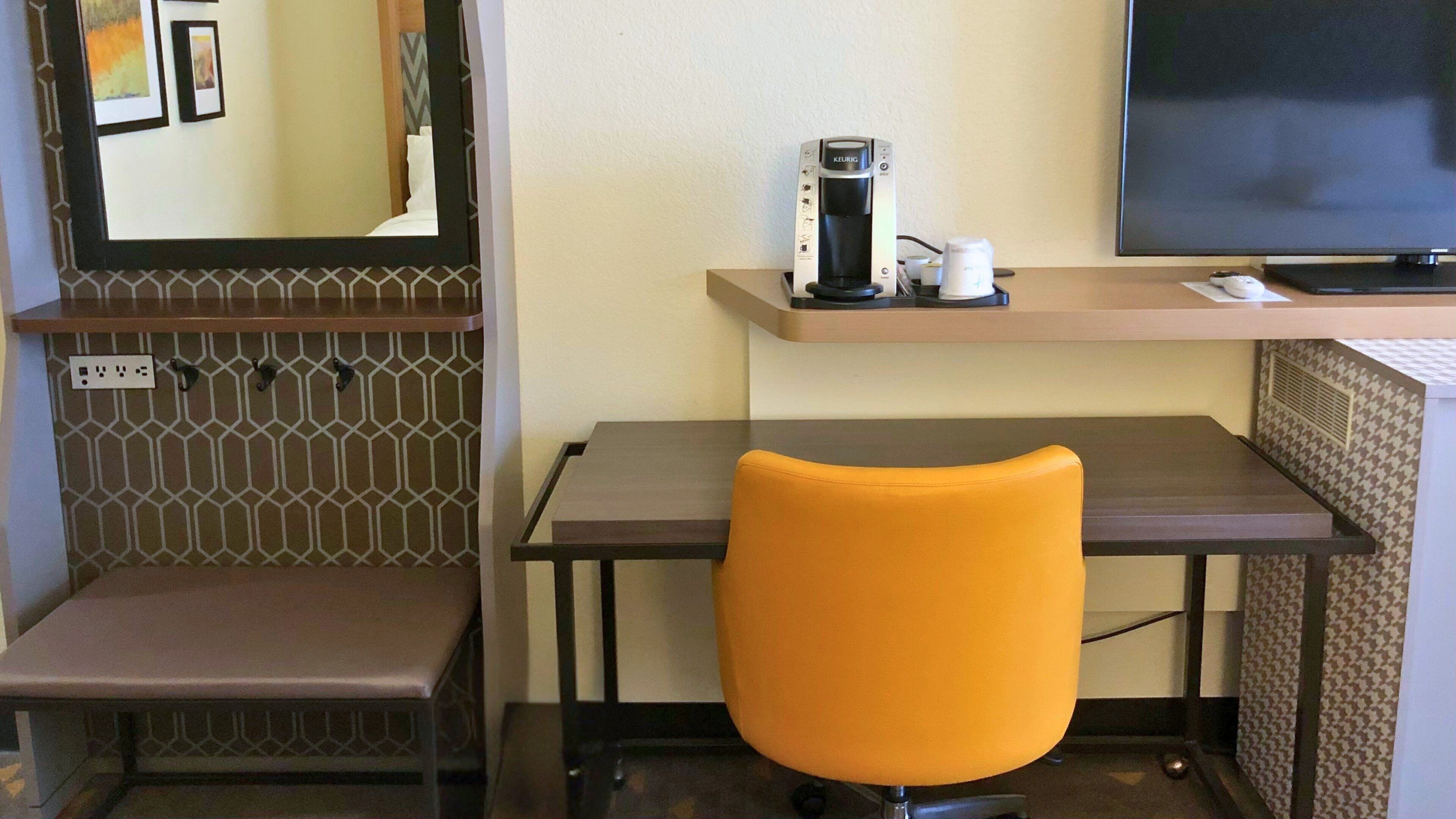 Una habitación de hotel con escritorio, silla, cafetera, televisor y espejo.