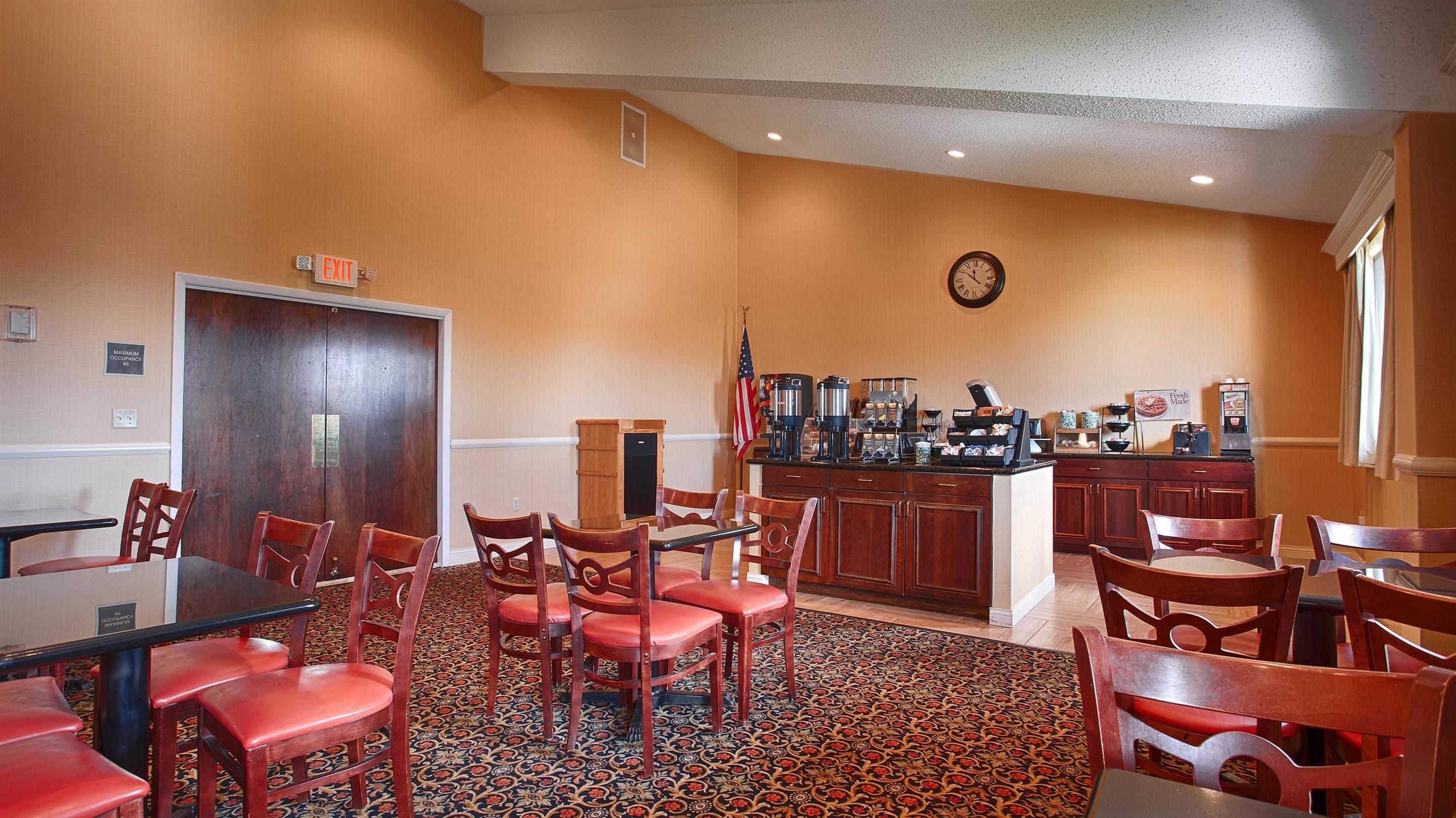 Un hall d’hôtel avec un coin café, une horloge au mur et un sol recouvert de moquette.