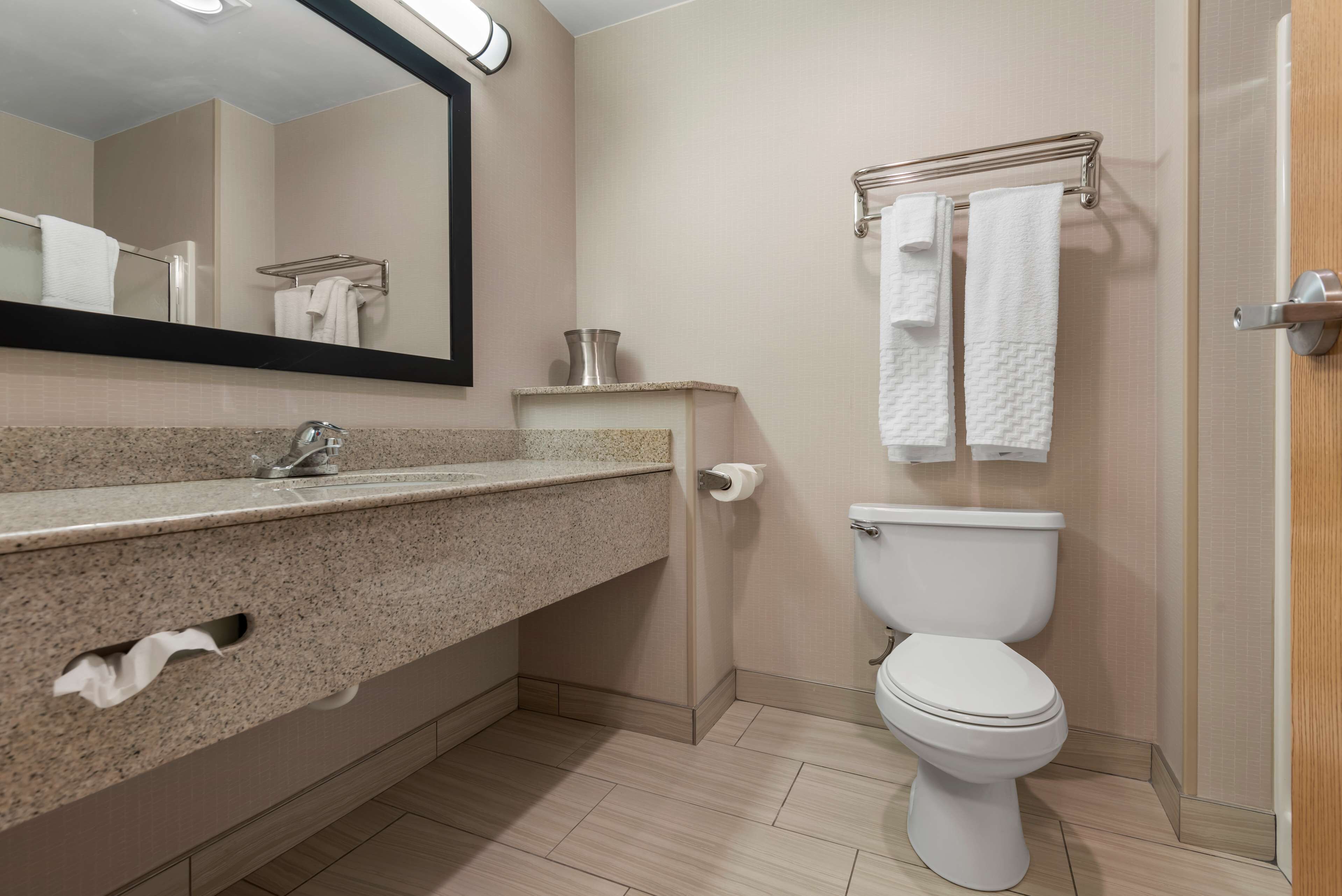 Un baño moderno con encimera de granito, inodoro blanco, toallero y espejo.