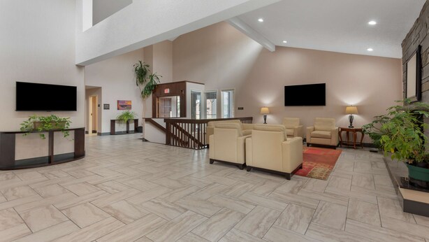 A spacious lobby with a high ceiling, a staircase, and a seating area with sofas and armchairs. - Best Western University Inn (Ithaca)